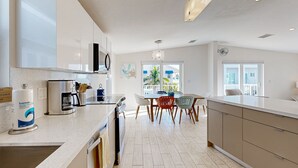 A modern kitchen with a central island, a dining area with chairs, and a large window providing natural light. - Modern waterfront home with balcony, patio, grill, W/D, & easy Atlantic access (Marathon)