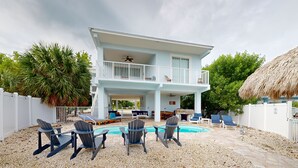 Ein zweistöckiges Haus mit Balkon, Pool und Sitzgelegenheiten im Freien.