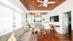 Un salon spacieux avec un plafond en bois, une grande télévision et un coin repas comprenant une table et des chaises.