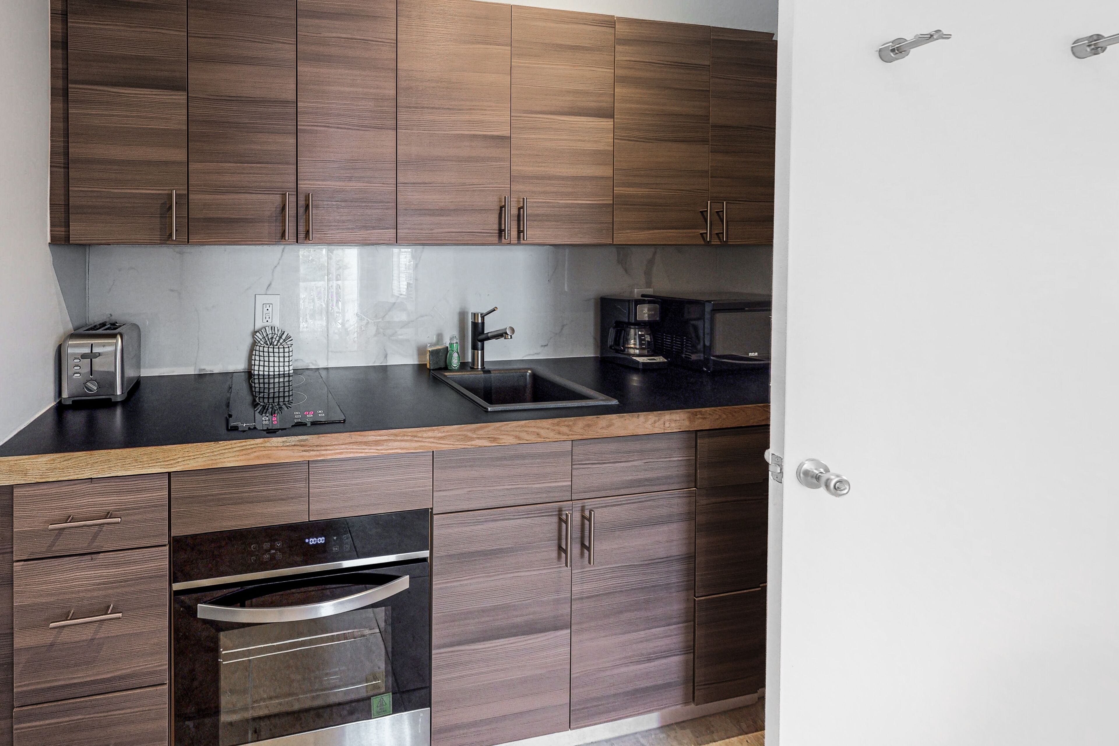 A modern kitchen with wooden cabinets, a black countertop, a built-in oven, and a coffee maker.