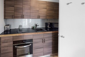 A modern kitchen with wooden cabinets, a black countertop, a built-in oven, and a coffee maker. - Cozy cottage apartment with front porch & upgraded finishes - close to beach (Key West)
