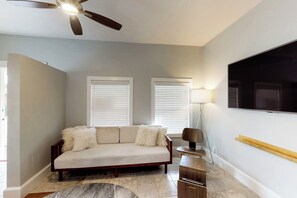 A living room with a sofa, a ceiling fan, two windows with blinds, a TV mounted on the wall, and a lamp. - Cozy cottage apartment with front porch & upgraded finishes - close to beach (Key West)