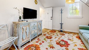 Ett rum med en vit vägg, en tv som hänger ovanför ett träskåp, en blommönstrad matta, en blå golvlampa och en grön soffa.