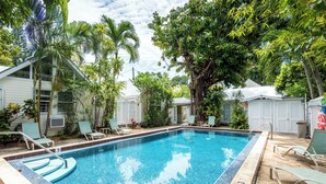 Ein Pool mit Liegestühlen, umgeben von Bäumen und einem Haus.