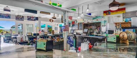 Un bar con mostrador de mármol, varias botellas y un cartel que dice 'Mejor beber con un Chingue de Pesca'.