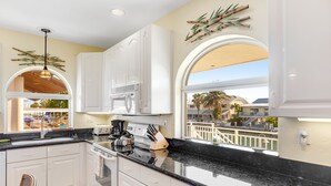 Una cocina moderna con armarios blancos, encimera negra y vistas a palmeras.