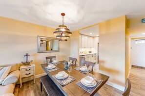 A dining room with a wooden table set for four, a hanging light fixture, and a kitchen in the background. - Wonderful Condo in Key West w/Free WiFi, Lanai, A/C, Shared Hot Tub & Pool (Key West)