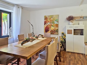 Ein Essbereich mit einem Holztisch, weißen Stühlen, einer dekorativen Tischmitte und einem großen, abstrakten Gemälde an der Wand.