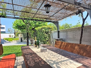 Eine Terrasss mit Holztisch, Stühlen und einer Pergola.