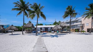 Un hôtel situé en bord de mer, doté d’une promenade en bois, de palmiers et de parasols en feuilles de palmier.