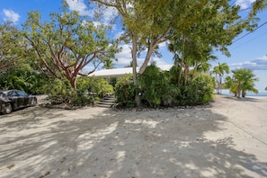 A beachfront property with a car parked on the left, a white building with a covered porch, and a sandy beach area.