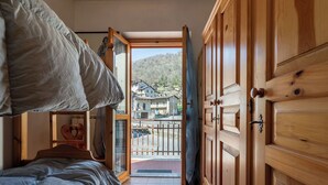Ein Schlafzimmer mit Bett, Holzschrank und Blick auf eine Wohngegend durch eine offene Tür.