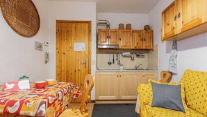 Eine kleine Küche mit Holzausstattung, einem Esstisch mit bunten Tischdecken und einem gelben Sofa mit gemustertem Bezug.
