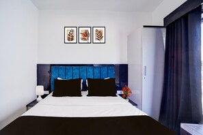 A hotel room with a bed, a nightstand, a lamp, a vase with flowers, and a refrigerator. - Deluxeisckon Temple Bhopal (Bhopal)