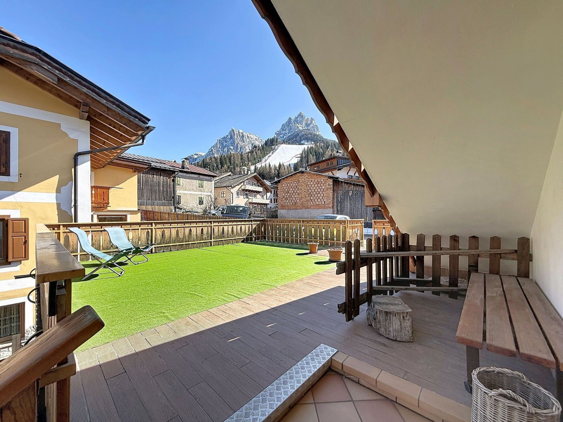 Eine Terrasse mit Holzdeck, einer Rasenfläche und Blick auf Berghäuser.