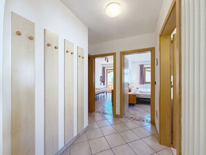 Ein Flur, der in ein Schlafzimmer mit Bett, Nachttisch und einem Vorhangfenster führt.