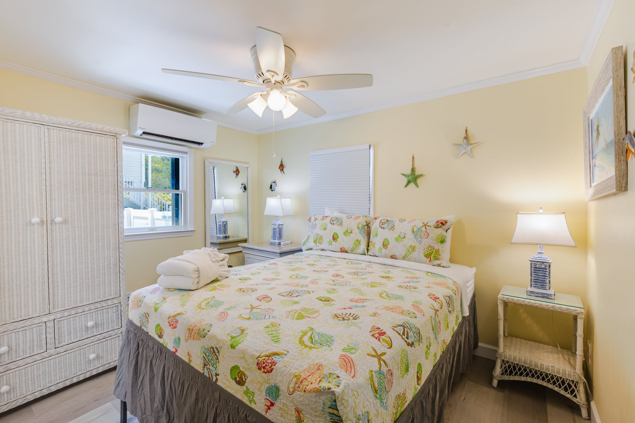 A bedroom with a bed, a ceiling fan, a window, a wardrobe, and a nightstand with a lamp.