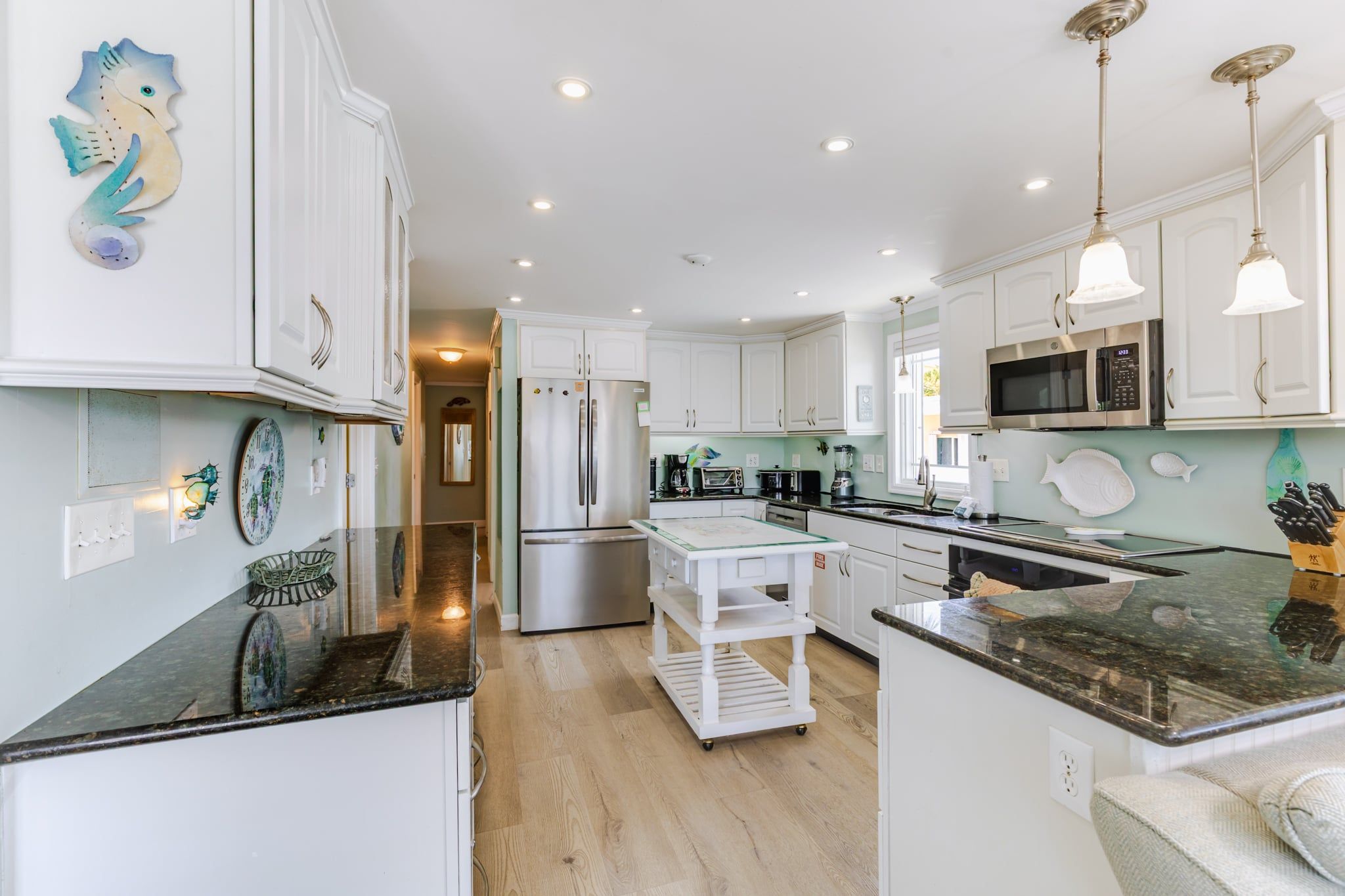 A modern kitchen with white cabinetry, a stainless steel refrigerator, a built-in oven, and a central island with a glass top.