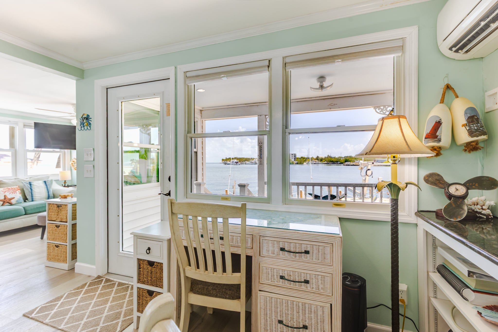 A room with a desk, chair, and a view of the water through large windows.