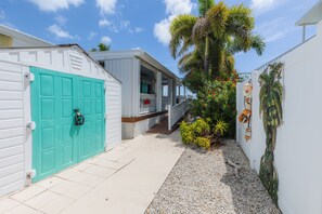 A pathway leading to a house with a turquoise door, a porch, and a small garden with palm trees and shrubs. - Dog-Friendly Home on the Water w/ Dock, Boat Access, Private Pool, & Free WiFi (Marathon)