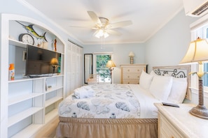 Une chambre à coucher comprenant un lit, une télévision, un ventilateur de plafond, une commode et une fenêtre.