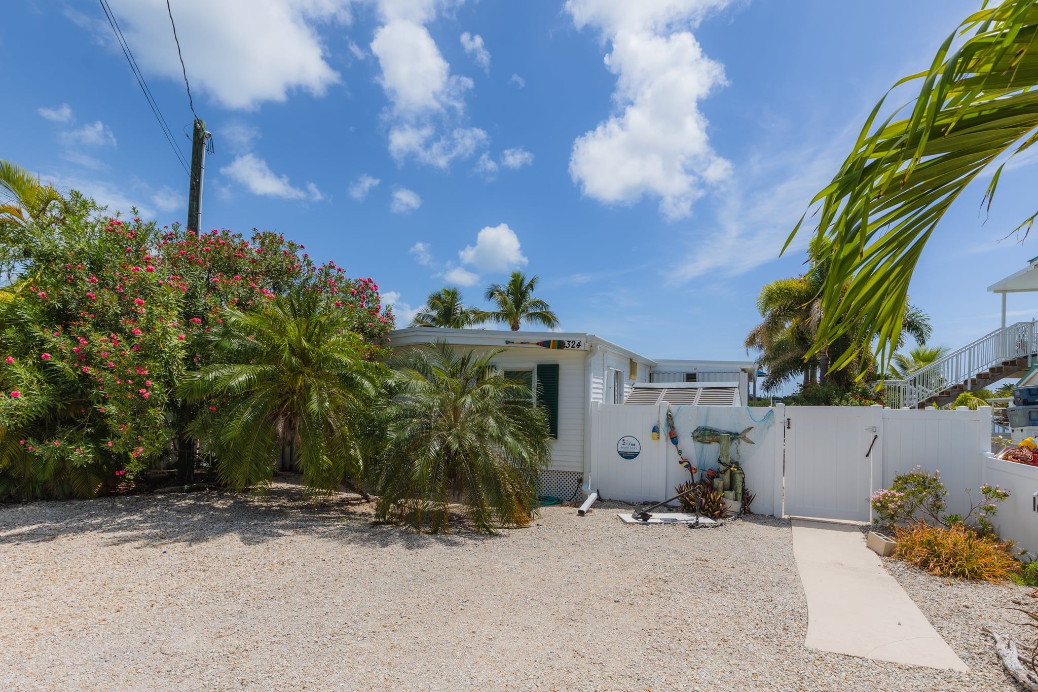 A residential property with a gravel driveway, a white house, and a palm tree.
