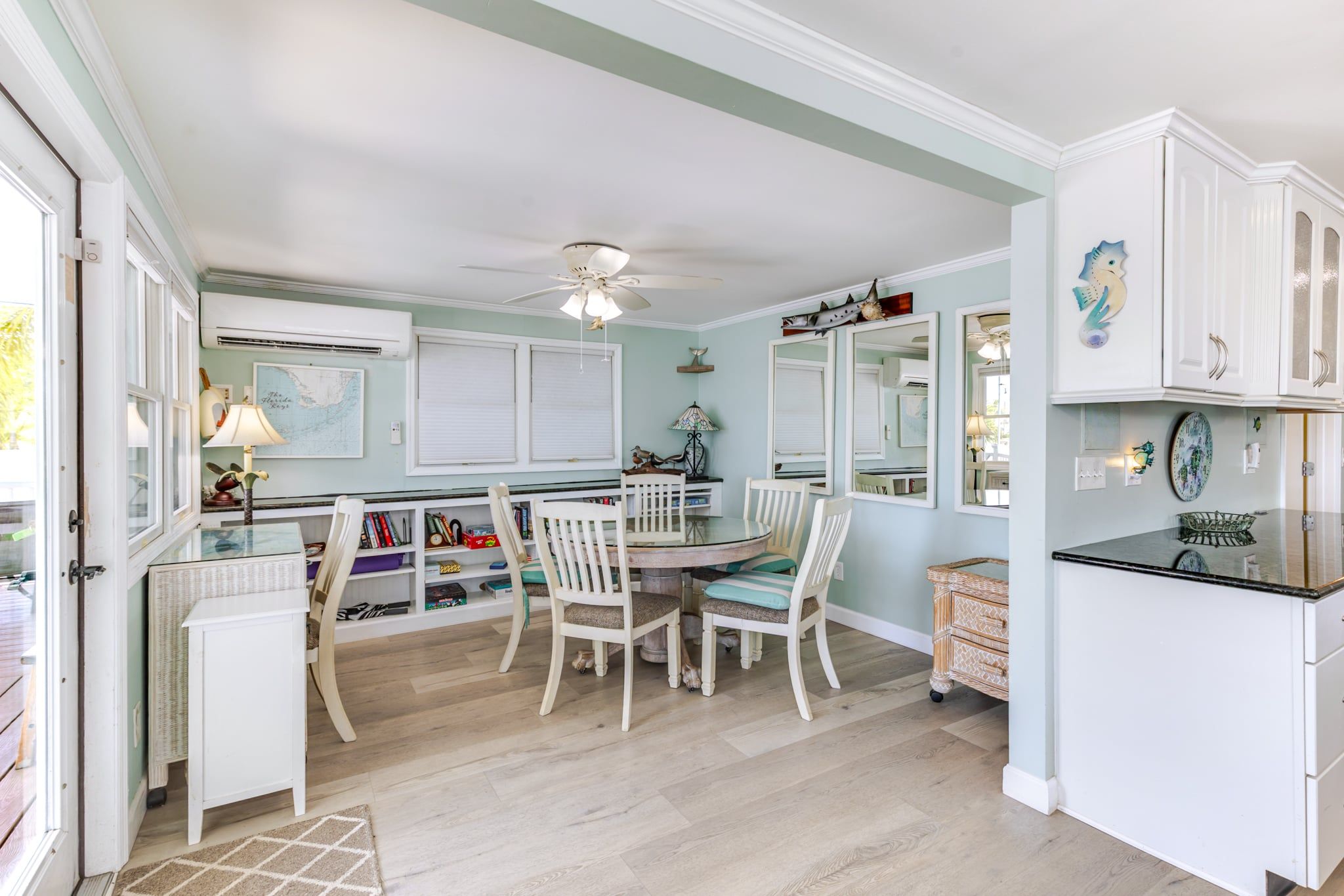 A kitchen with white cabinetry, a dining table with chairs, a ceiling fan, and a window with blinds.
