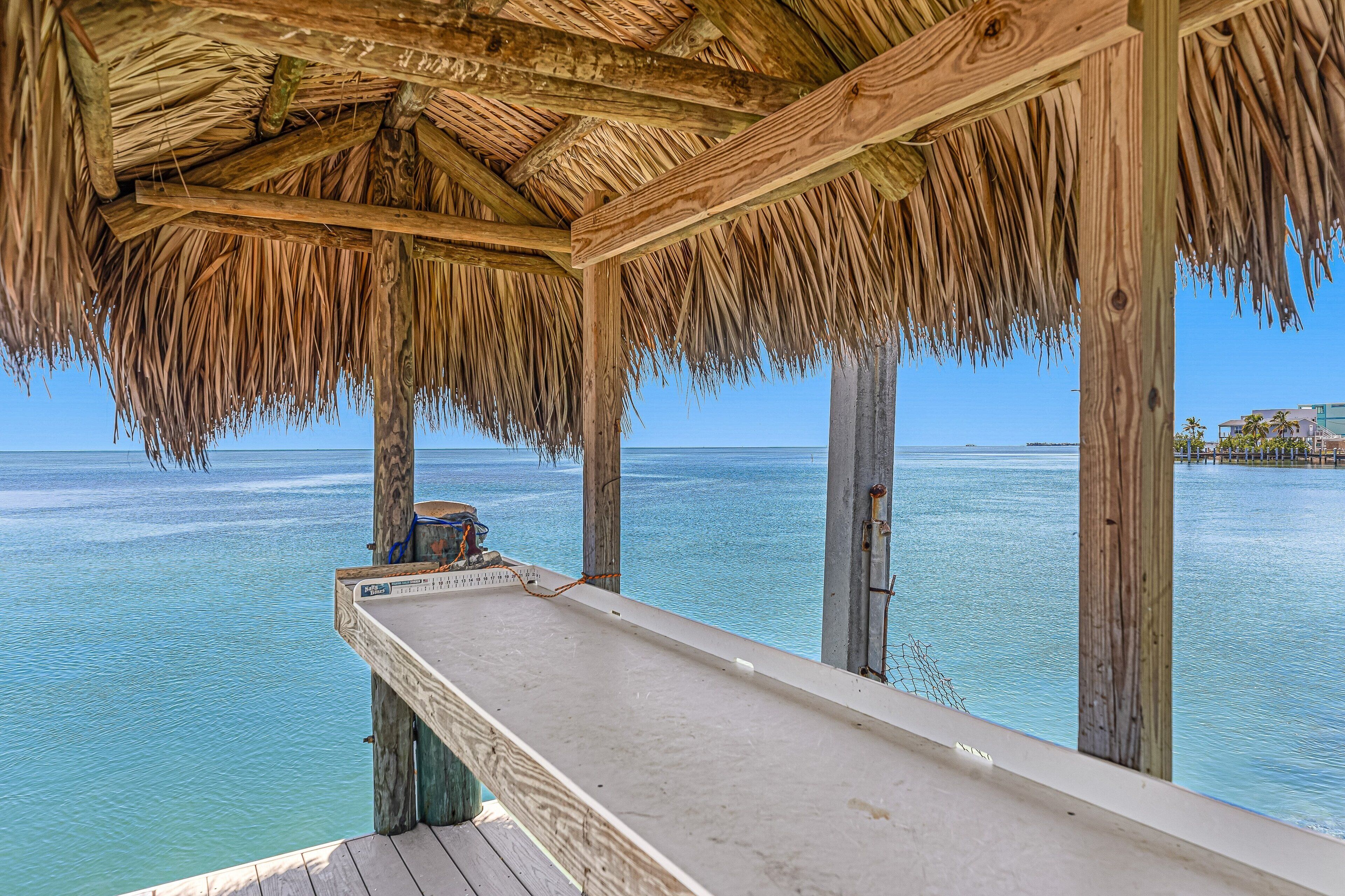 Een houten terras met rieten dak met uitzicht op turquoise water.