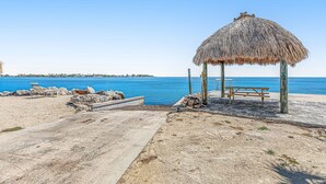 A beach with a thatched-roof structure, a wooden bench, and a concrete pathway leading to the water. - Snowbird-friendly condo in oceanfront complex with heated pool, BBQ, W/D, AC (Marathon)