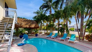 A swimming pool with lounge chairs, a thatched roof structure, and palm trees. - Private pool, boat dock, water view, canal front, fully equipped kitchen (Marathon)