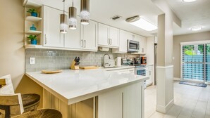 A modern kitchen with white cabinets, a large island, stainless steel appliances, and pendant lighting. - Beautiful, sunlit home with pool, tennis court & beach access - near the marina (Islamorada)