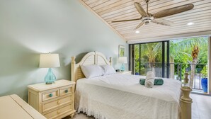 A bedroom with a bed, nightstands, a ceiling fan, and a view of greenery outside. - Beautiful, sunlit home with pool, tennis court & beach access - near the marina (Islamorada)