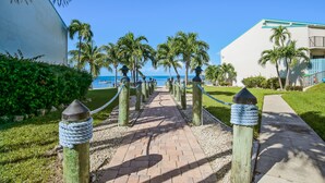 A paved pathway lined with wooden posts and ropes, leading to a building with a view of the ocean. - Beautiful, sunlit home with pool, tennis court & beach access - near the marina (Islamorada)