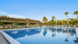 A swimming pool with a thatched-roof structure, palm trees, and a fenced area with lounge chairs. - Beautiful, sunlit home with pool, tennis court & beach access - near the marina (Islamorada)