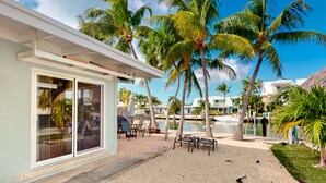 A modern building with large sliding glass doors, outdoor seating, palm trees, and a pool area.