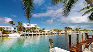 A marina with boats, a dock, and a waterfront view of a resort with multiple buildings and palm trees.