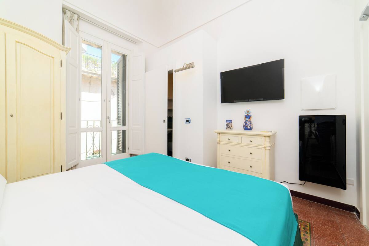 A hotel room with a bed, a TV, a dresser, and a door leading to a balcony.