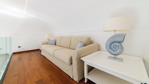 A modern living room with a beige sofa, a white side table, and a spiral lamp. - AMALFI GALLERY (Amalfi)