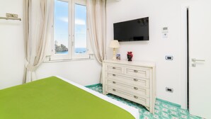 A bedroom with a bed, a dresser, a TV, and a window with curtains. - AMALFI GALLERY (Amalfi)