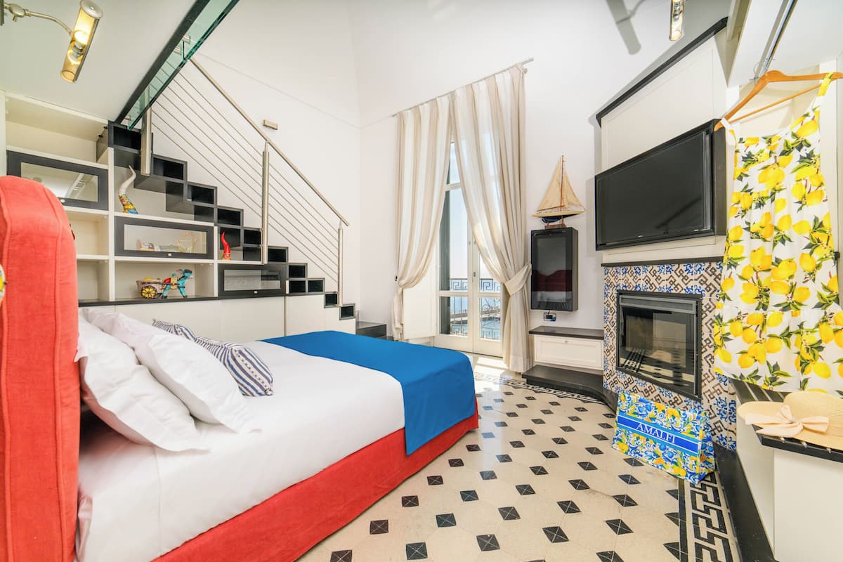 A hotel room with a bed, a TV, a fireplace, a staircase, and a view of the outside.