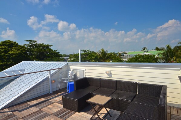 A rooftop patio with a seating area, a small table, and a blue trash bin. - Fresh Getaway w/ Private Pool & Rooftop Patio - Great Location, Steps from Beach (Key West)