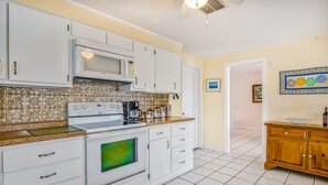 A kitchen with white cabinets, a microwave, and a stove. There is a wooden cabinet to the right and a tiled backsplash. - Waterfront, Single-Story Home on a Canal w/ Dock, Kayaks, AC - 1 Small Dog OK (Key West)
