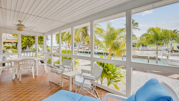 A covered outdoor area with white furniture, a pool, and a view of the water and greenery. - Waterfront, Single-Story Home on a Canal w/ Dock, Kayaks, AC - 1 Small Dog OK (Key West)