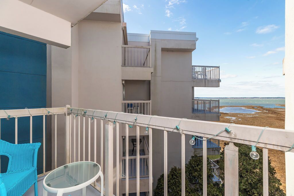 Ein Balkon mit einem Glastisch und einem blauen Stuhl, mit Blick auf ein Gebäude mit mehreren Balkonen und Meerblick.