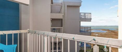 Ein Balkon mit einem Glastisch und einem blauen Stuhl, mit Blick auf ein Gebäude mit mehreren Balkonen und Meerblick.