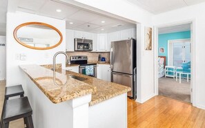 A modern kitchen with white cabinetry, a granite countertop, stainless steel appliances, and a small island with a sink. - Lovely 3 Bedroom with great bay views, outdoor pool, and just steps to the beach. Vacation at the Shore with Shoreline Properties (Ocean City)