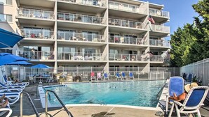Un hotel a più piani con balconi, piscina e lettini prendisole.