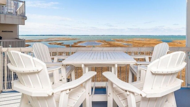 Un balcone con un tavolo e quattro sedie, con vista su una spiaggia e l'oceano, e sulla costa in lontananza.