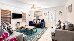 Ein Wohnzimmer mit einer Couch, einem Couchtisch, einem Fernseher und einem Deckenventilator.