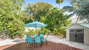 Eine Holzterrasse mit Tisch und Stühlen, umgeben von Bäumen und einem Schuppen.